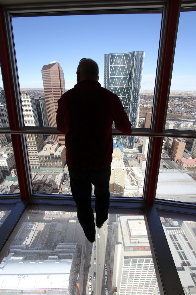 A visitor to the Calgary Tower stands on glass and ponders downtown Calgary.