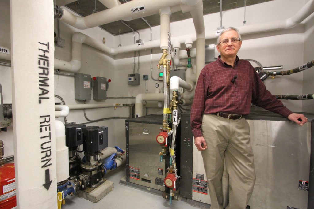 Leigh Bond in the mechanical room of the Brentwood Apartments next to the two large heat pumps which provide all of the space heating and backup hot water heating for the 29 unit affordable housing complex. 