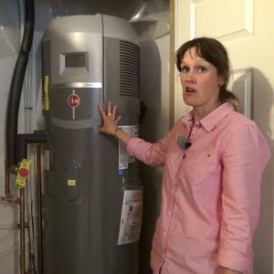 Jennifer Weatherston shows the Rheem air source heat pump/electric hybrid water heater uses solar electricity to run the heat pump (like a fridge working in reverse) and if it has trouble keeping up this unit also has electric coil heaters as a back up heat source for producing hot water very efficiently in a solar powered home. Photo David Dodge, GreenEnergyFutures.ca